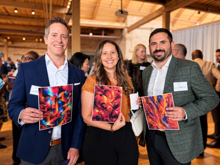 Three event attendees smiling and holding printed AI artwork created from their voices