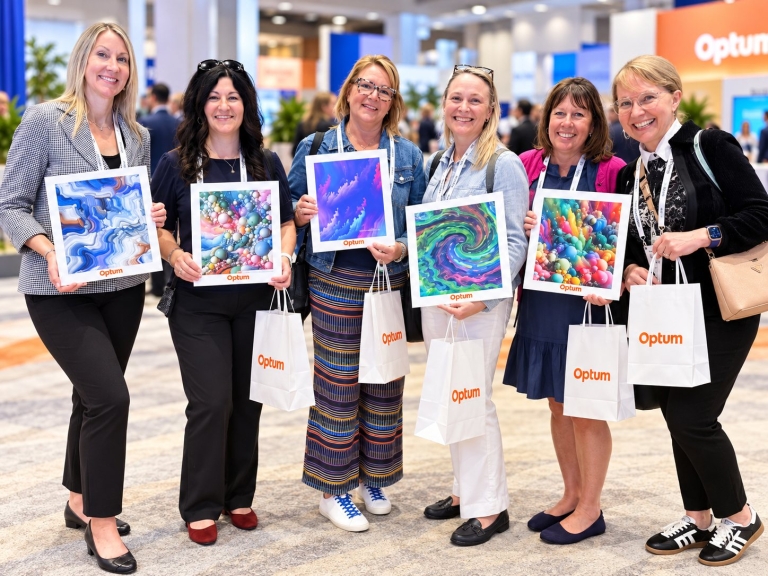 Six SCOPE 2026 attendees holding printed voice-to-art artwork and Optum tote bags on the exhibit floor